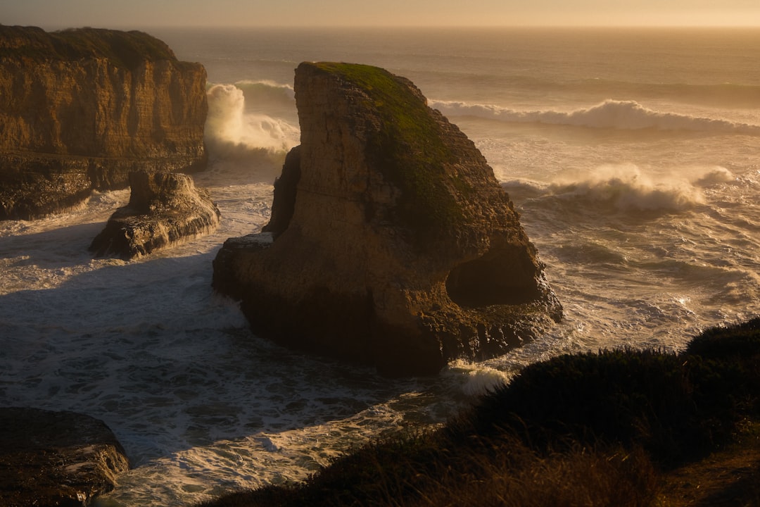 Waves crash against rocky coastal formations at sunset.